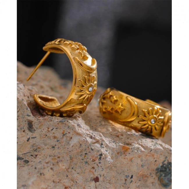 Gold hoop earrings with intricate designs on a textured surface