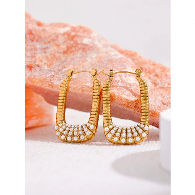 Gold hoop earrings with a textured ribbed design and rows of small white faux pearls at the bottom, displayed on a white surface with a pink rock prop in the background.