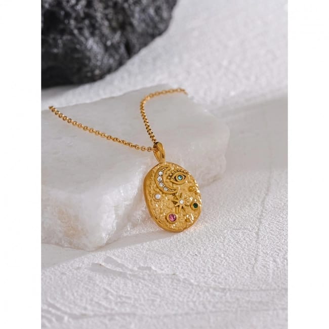 Gold necklace with a decorative pendant on a textured white surface